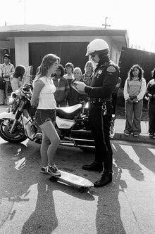  A girl getting a ticket for skateboarding, when it was illegal, in Redondo Beach California in the 1970s, in black and white, by SPOT