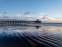  Color photo of the Manhattan Beach pier at a very low tide, with repeating ripples of sand in the foreground.
