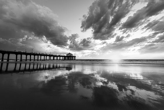 Manhattan Beach pier at sunset with a low tide and reflection of the pier and clouds, in black and white