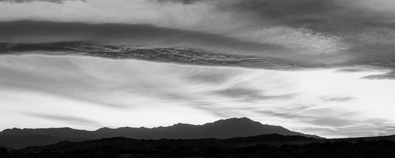 panoramic photograph taken during sunset in the desert in Palm Springs featuring clouds and a mountain range, in black and white