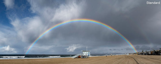 A panoramic photograph of a rainbow on both sides of a lifeguard tower in manhattan beach, california