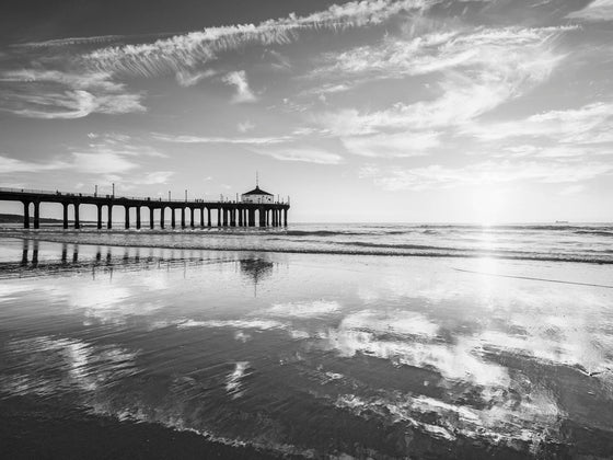 manhattan beach pier at sunset with a low tide and clouds reflecting in the sand, in black and white