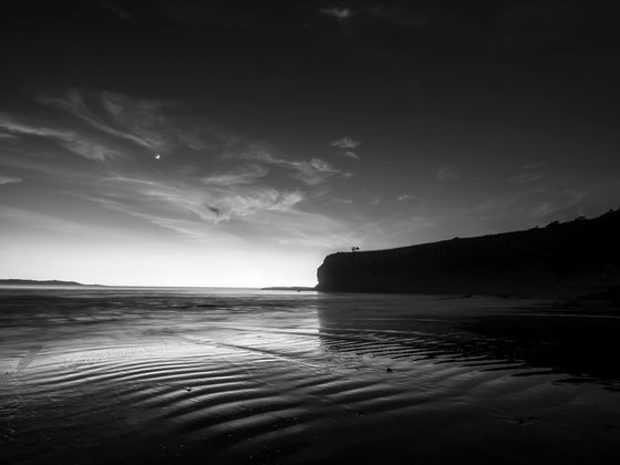 Palos Verdes sunset with blue skies, wispy pink clouds, and a nice reflection in the rippled sand in black and white.