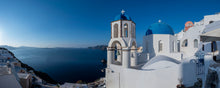  A panoramic photograph that features the horizon of Oia in Sanotrini, specifically focusing on the white and blue church