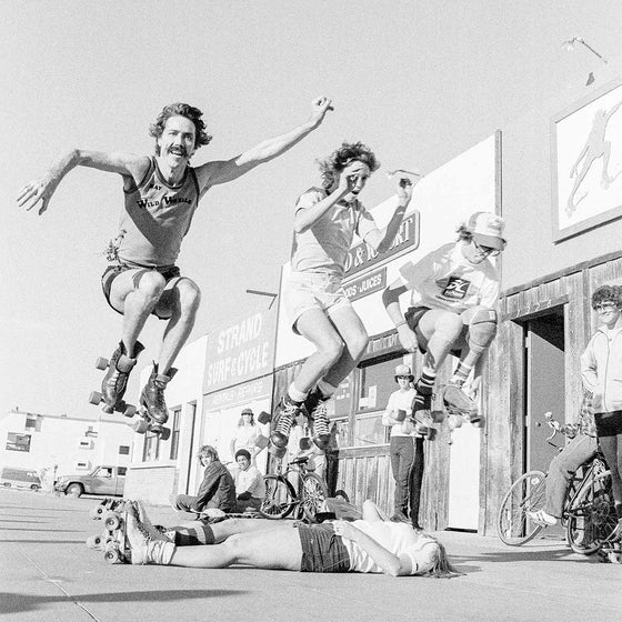 Rollerskaters jumping people laying down on the Strand, in Hermosa Beach, Los Angeles in the 1970s.  Photo by SPOT.  Ray Tate is on the left and Fred Blood is on the right.  This is a black and white photo.