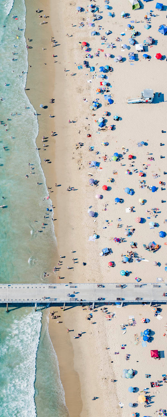 Vertical color aerial photo of Hermosa Beach in Los Angeles with beach umbrellas, sand, ocean, a lifeguard tower, and the Hermosa Beach pier