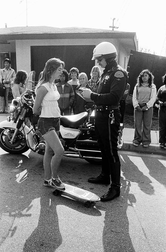 A girl getting a ticket for skateboarding, when it was illegal, in Redondo Beach California in the 1970s, in black and white, by SPOT
