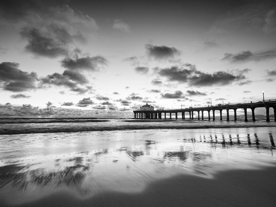 Manhattan Beach California pier at sunset at low tide, with the clouds reflecting in the sand, in black and white