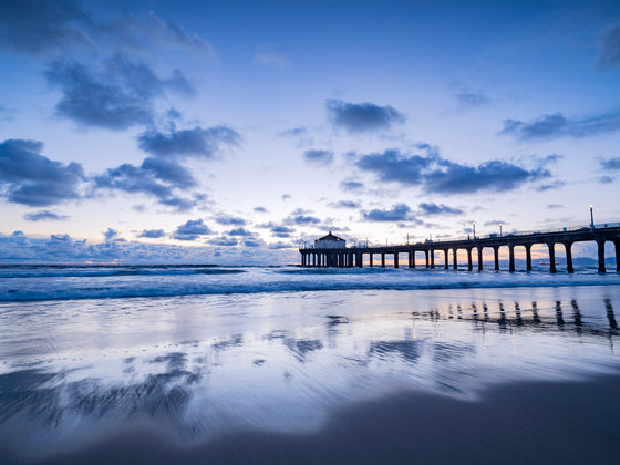 Manhattan Beach California pier at sunset at low tide, with the clouds reflecting in the sand, and a cool blue tone