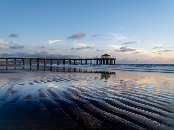 Color photo of the Manhattan Beach pier at a very low tide, with repeating ripples of sand in the foreground.