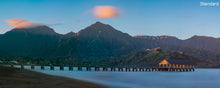  Panoramic photo of Hanalei Bay Pier in Kauai Hawaii with blue water and a blue sky and pink clouds at sunrise with the Napali Coast in the background