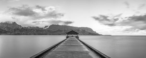 Black and white panoramic photo of Hanalei Bay Pier in Kauai Hawaii with clouds with the Napali Coast in the background
