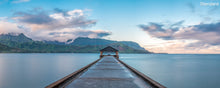  Panoramic photo of Hanalei Bay Pier in Kauai Hawaii with blue water and a blue sky and clouds with the Napali Coast in the background