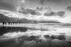 A photograph taken at sunset of Hanalei bay featuring the Hanalei pier, in black and white