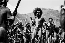  A warrior in Irian Jaya with a spear in his hand with warriors in the background. in black and white.