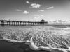 Manhattan Beach pier at low tide, sunset, with the foamy water in the foreground, in black and white