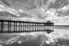 Manhattan Beach California Pier with clouds and a blue sky reflected in the sand at low tide right before sunset, in black and white