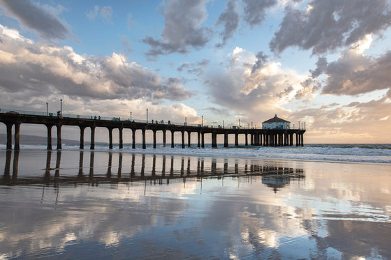 Manhattan Beach California Pier with clouds and a blue sky reflected in the sand at low tide right before sunset