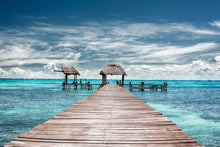  A wooden dock from the coast of Isla Mujeres that highlights the blue Caribbean ocean in the background with a sky full of whimsical clouds.