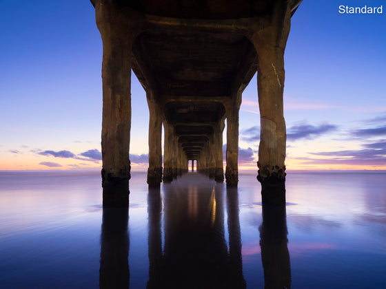 Manhattan beach pier at sunset with blue skies and a reflection of the pier and clouds in the sand at low tide
