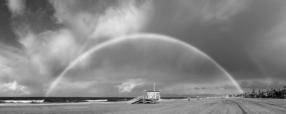 A panoramic photograph of a rainbow on both sides of a lifeguard tower in manhattan beach, california in black and white