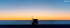 A panoramic photo of a lifeguard tower in Hermosa Beach / Manhattan Beach (Los Angeles California) at sunset with golden ad blue skies over the Pacific Ocean.