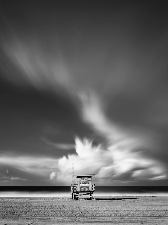 A photo of a lifeguard tower in Manhattan Beach (Los Angeles California) with dramatic clouds overhead, in black and white