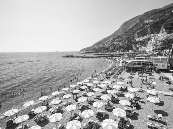 Black and white image of beach umbrellas at the Amalfi Beach Club beach with the Mediterranean ocean and some of the mountain hills in the background on the right side.