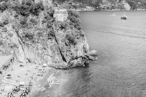 Black and white photo of the Amalfi Coast with a small beach and a Beach Club with the cliff for the brave to cliff dive.