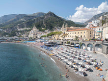 Colorful image of the beautiful Amalfi town on the Amalfi coast in Italy with water, beach clubs and umbrellas with the mountains in the background. 