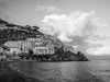 Amalfi Coast houses on the hillside with big white clouds with the Mediterranean Ocean in the foreground.