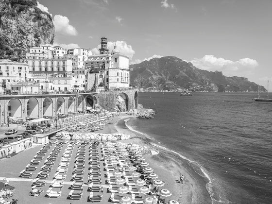 Atrani beach with sun beds and umbrellas on the Amalfi coast in Italy on a sunny day in black and white.