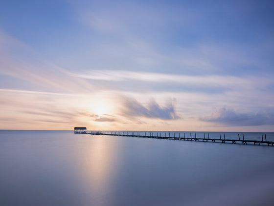 A photograph of a dock in the ocean during sunrise with a calm sky and calmer sea on Cuba's northern coast