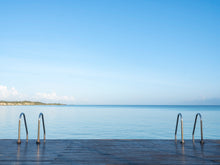  A close-up photo of a dock with two handle-bars in the Caribbean with crystal clear blue water and ripples in the ocean below the dock.