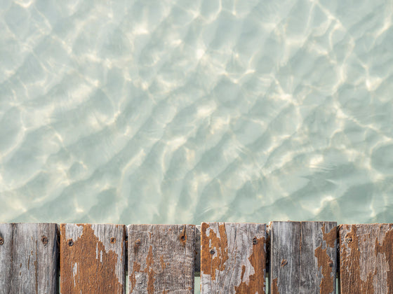 A close-up photo of a dock in the Caribbean with crystal clear water and ripples in the sand below it.
