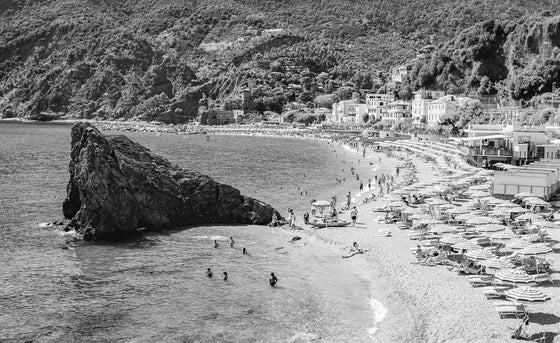 Black and white photo of Eden Rock in Monterosso Cinque Terre , Italy beach umbrellas with water and the tree covered hills in the background
