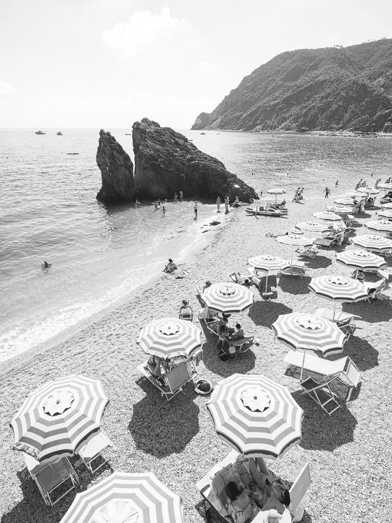 Monterosso beach with the big rock and striped umbrellas on the beach in black and white.