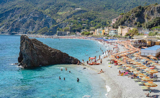 Eden Rock in Monterosso Cinque Terre , Italy orange and green beach umbrellas with turquoise water and lush greenery on the hills as a background
