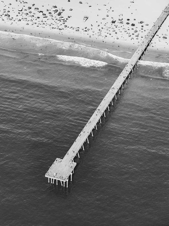 Black and white aerial photo of Hermosa Beach Pier in Los Angeles with beach umbrellas and a lifeguard tower