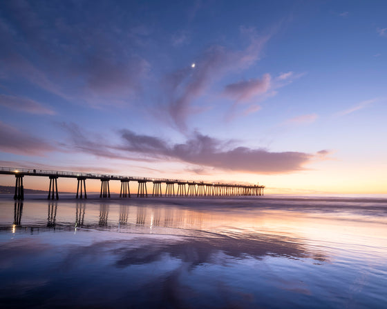 Sunset at Hermosa Beach California pier, low tide, with the clouds reflecting in the sand, and a moon present above the pier