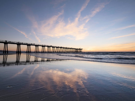 Hermosa Beach California pier, at sunset, with clouds reflected on the sand in the beach