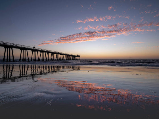 Hermosa Beach pier at sunset with clouds reflecting in the sand