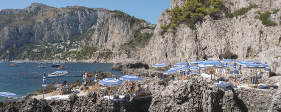 panoramic photo of La Fontelina beach club in Capri Italy with sunbathers and blue and white umbrellas