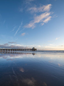 The Manhattan Beach California pier with blue skies and clouds, at low tide, with the clouds reflected in the sand