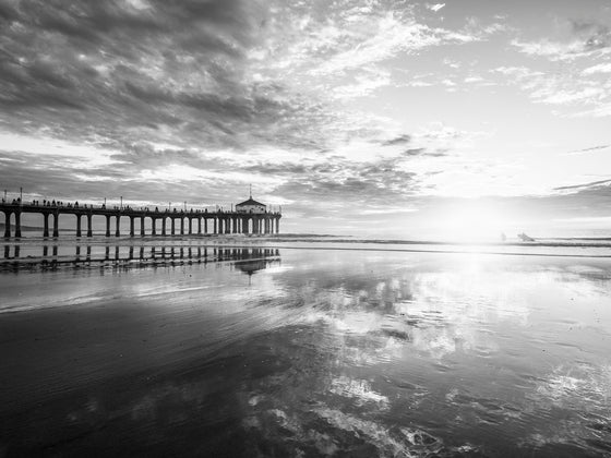 Manhattan Beach pier at low tide at sunset, with the sky reflecting in the sand at low tide, with two surfers, in black and white