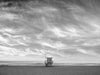 A Manhattan Beach lifeguard tower, in Los Angeles, at sunrise, with soft clouds over the Pacific Ocean, in black and white