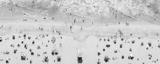 Black and white aerial photo of Manhattan Beach in Los Angeles with a lifeguard tower, beach umbrellas, sand and the ocean