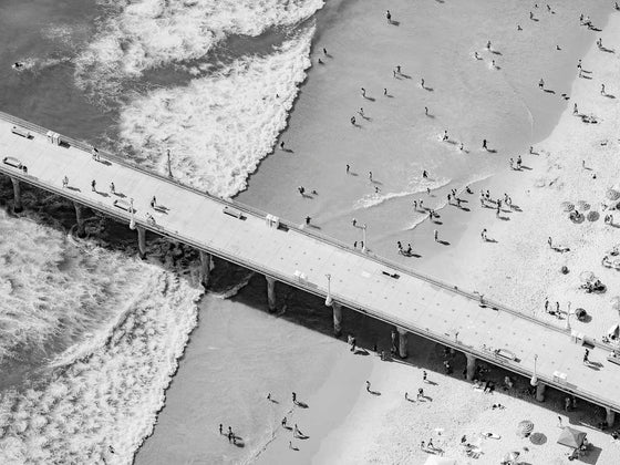 Black and white aerial photo of Manhattan Beach Pier in Los Angeles with beach umbrellas, sand and the ocean