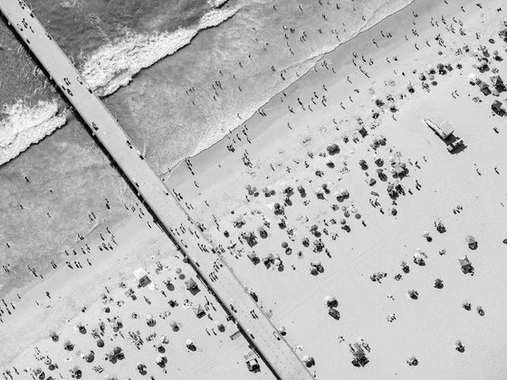 Black and white aerial photo of the Manhattan Beach Pier in Los Angeles with beach umbrellas, a lifeguard tower and the ocean