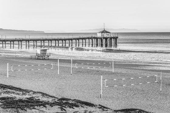 Sunrise over the Pacific Ocean at the Manhattan Beach Pier, with surfers and a small swell and decent surf, in black and white